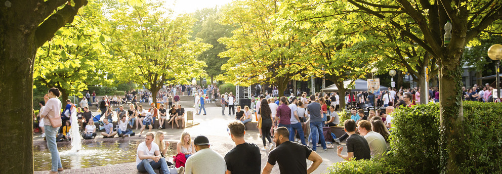 Sommerfest Viele Personen halten sich rund um einen Brunnen auf. Dieser ist umgeben von Bäumen.
